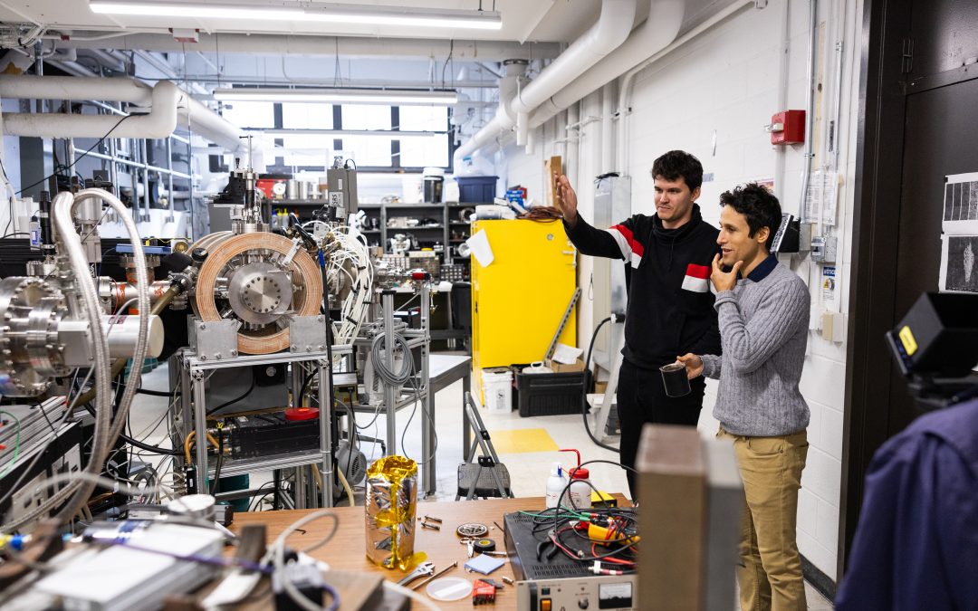 Two men at right side standing in lab with lots of large scientific equipment