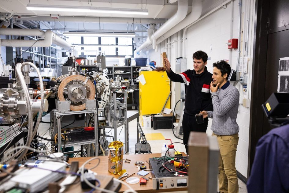 Two men at right side standing in lab with lots of large scientific equipment