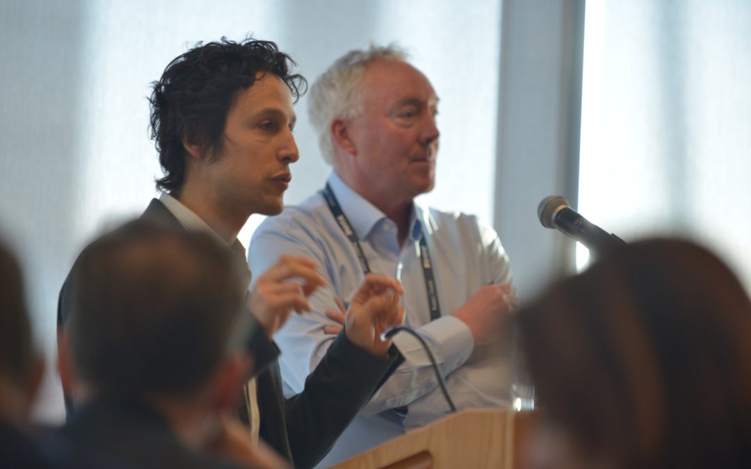 David Cohen-Tanugi at podium with Dennis Whyte in background, both men viewed from side as they speak to audience.